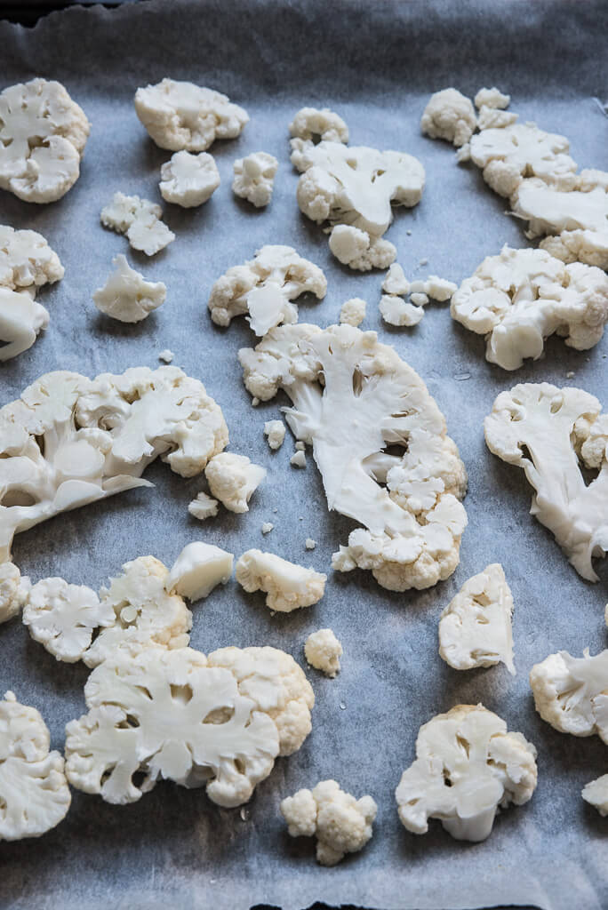 cauliflower steaks and florets on a lined baking sheet